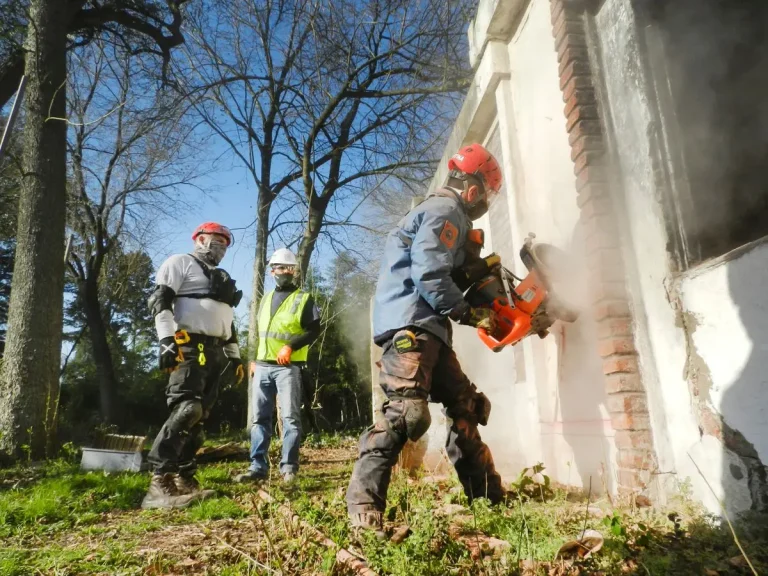 Demolition crew in safety gear taking down a brick wall with machinery